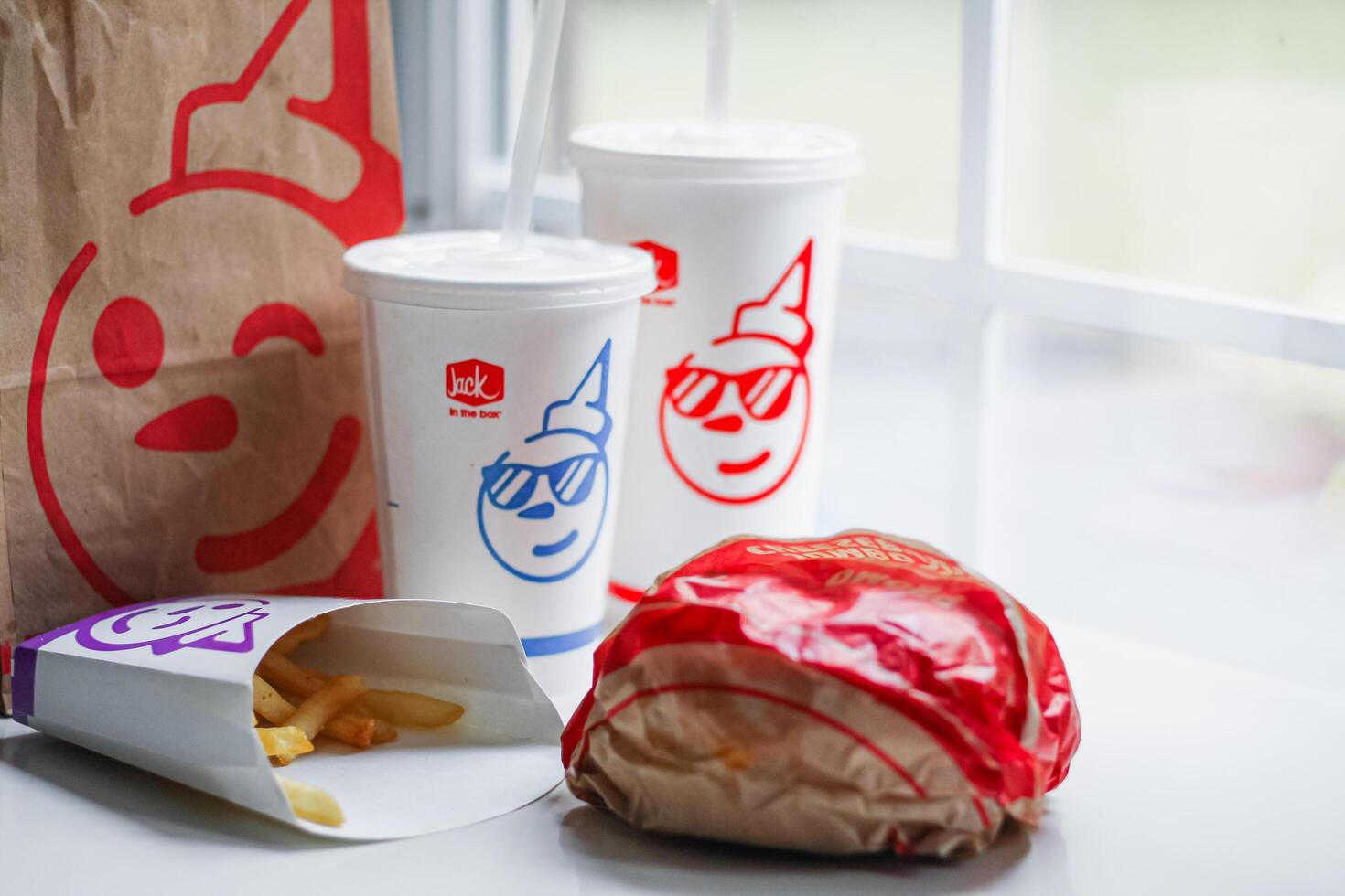 WASHINGTON, USA - August 08, 2024 - A table setting featuring a fast food order from Jack in the Box. The meal includes two white styrofoam cups with red lids and straws, and a wrapped burger. photo
