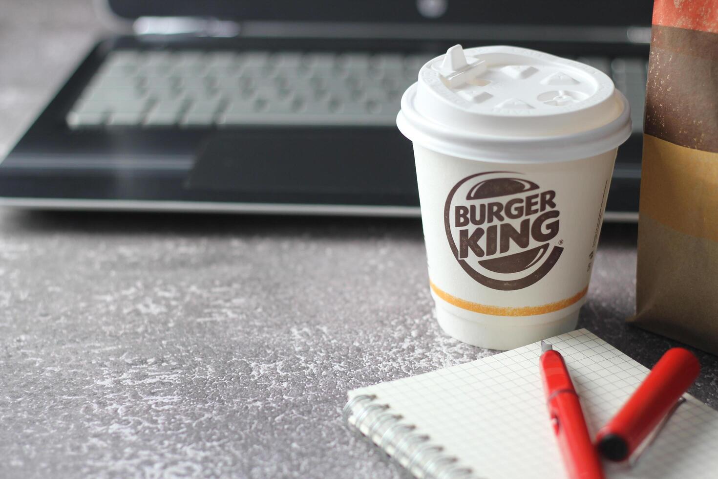 WASHINGTON - USA - August 17, 2024 - A close-up of a Burger King coffee cup, with a laptop and a paper bag in the background. photo