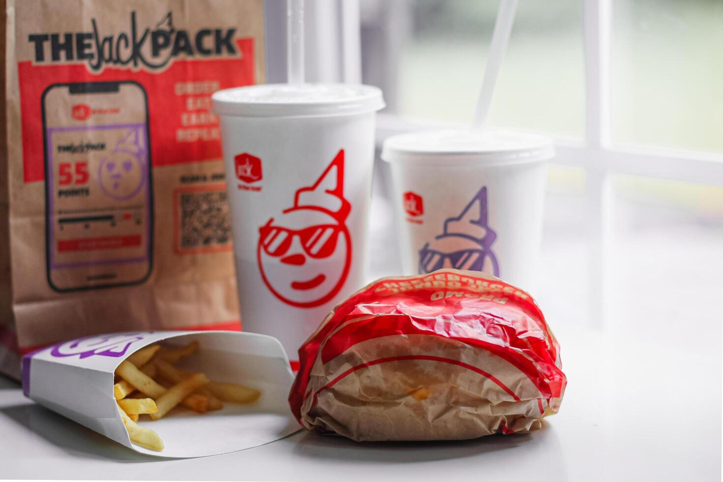 WASHINGTON, USA - August 08, 2024 - A table setting featuring a fast food order from Jack in the Box. The meal includes two white styrofoam cups with red lids and straws, and a wrapped burger. photo