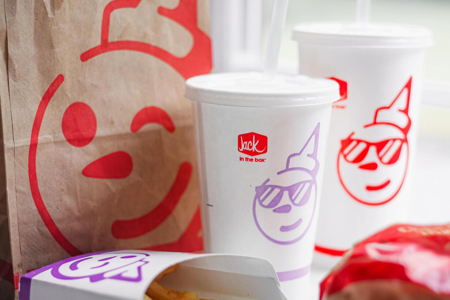 WASHINGTON, USA - August 08, 2024 - A table setting featuring a fast food order from Jack in the Box. The meal includes two white styrofoam cups with red lids and straws, and a wrapped burger. photo