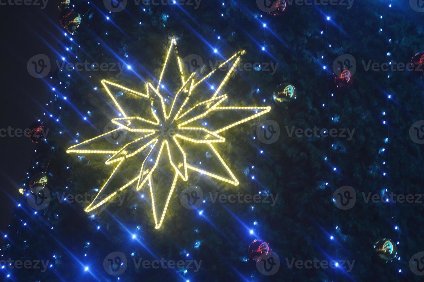 Glowing snowflake, Christmas star on blue festive lights of tree. Festive New Year background. Modern illumination on city street photo