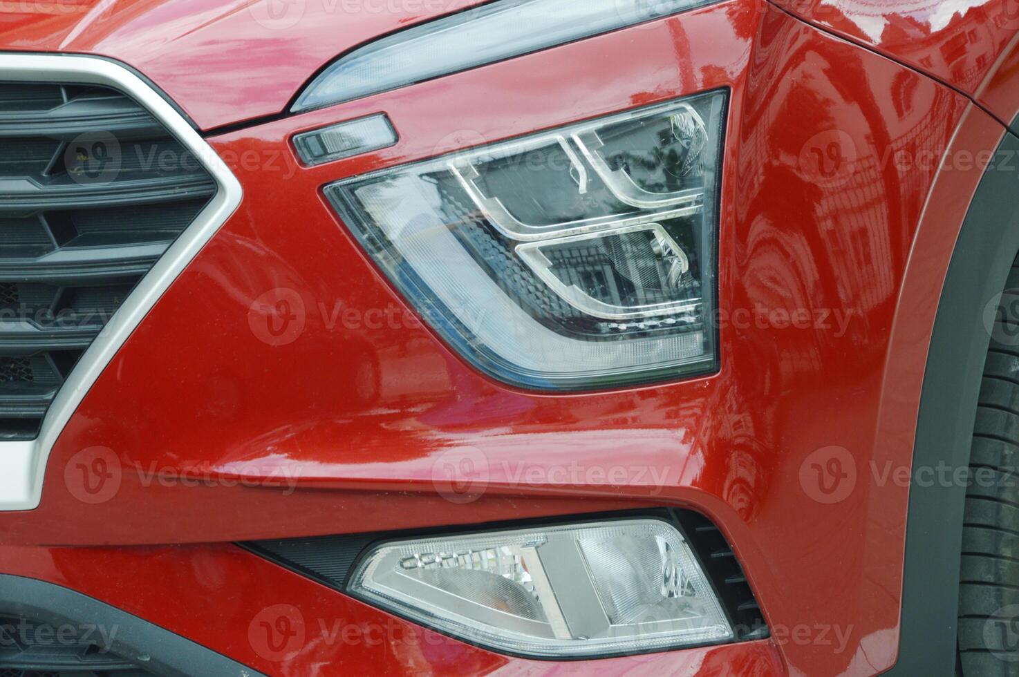 A fragment of the body of a modern red passenger car - the front headlight and part of the hood. photo