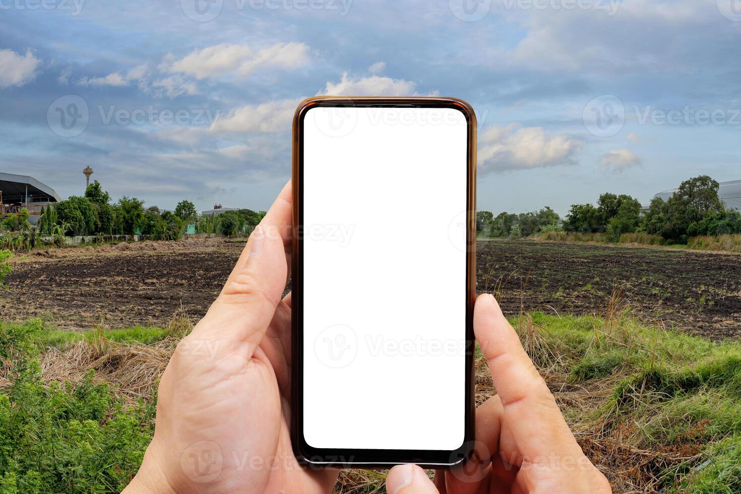 Cropped image of businessman using smartphone. Empty dry cracked swamp reclamation soil, land plot for housing construction project and beautiful blue sky. photo