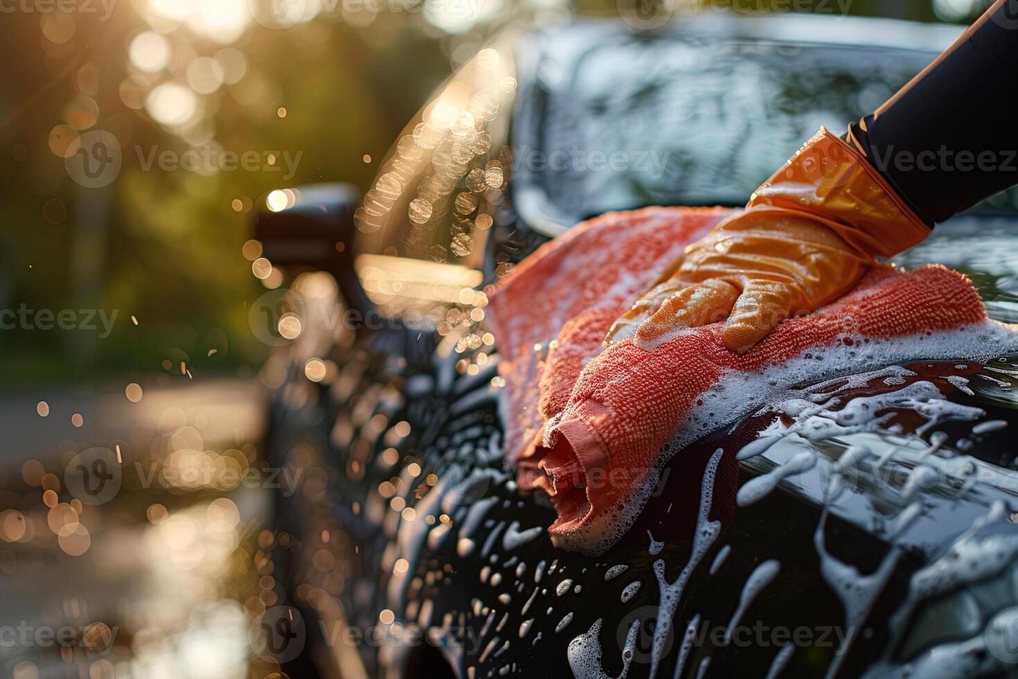 closeup of gloved hand washing black car with red rag and detergent with foam photo