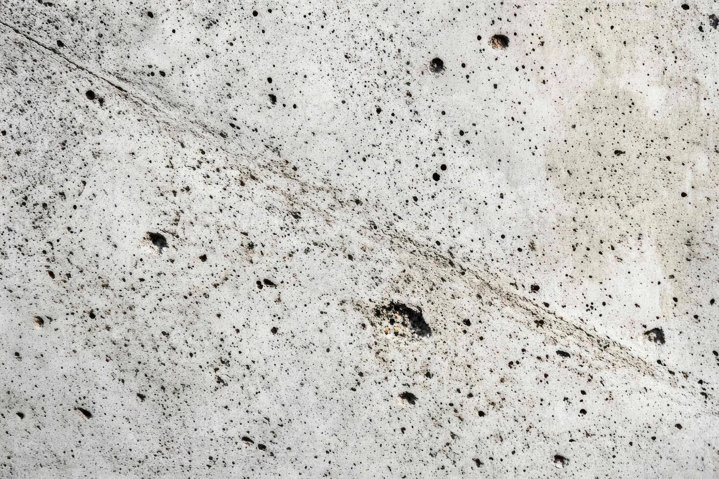 Close-up of a White and Gray Textured Wall with a Diagonal Crack and Pockmarks photo