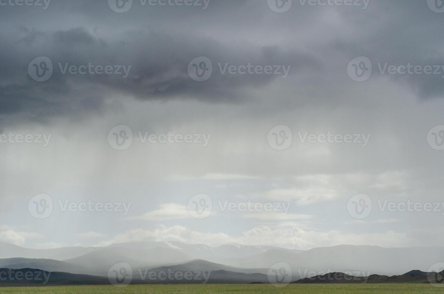 Rays of light shine down from a cloudy sky into a fields. Sun beams bursting through raining clouds over a fields. mountains against the background of rain in the distance. Background for text photo