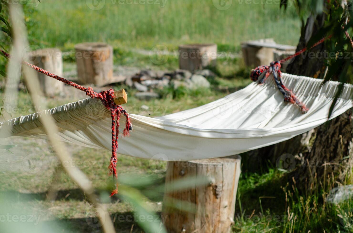 The edge of a hammock among the greenery. The white fabric of the hammock is suspended in the greenery of the garden. Fragment of a hammock for relaxation in a green garden photo