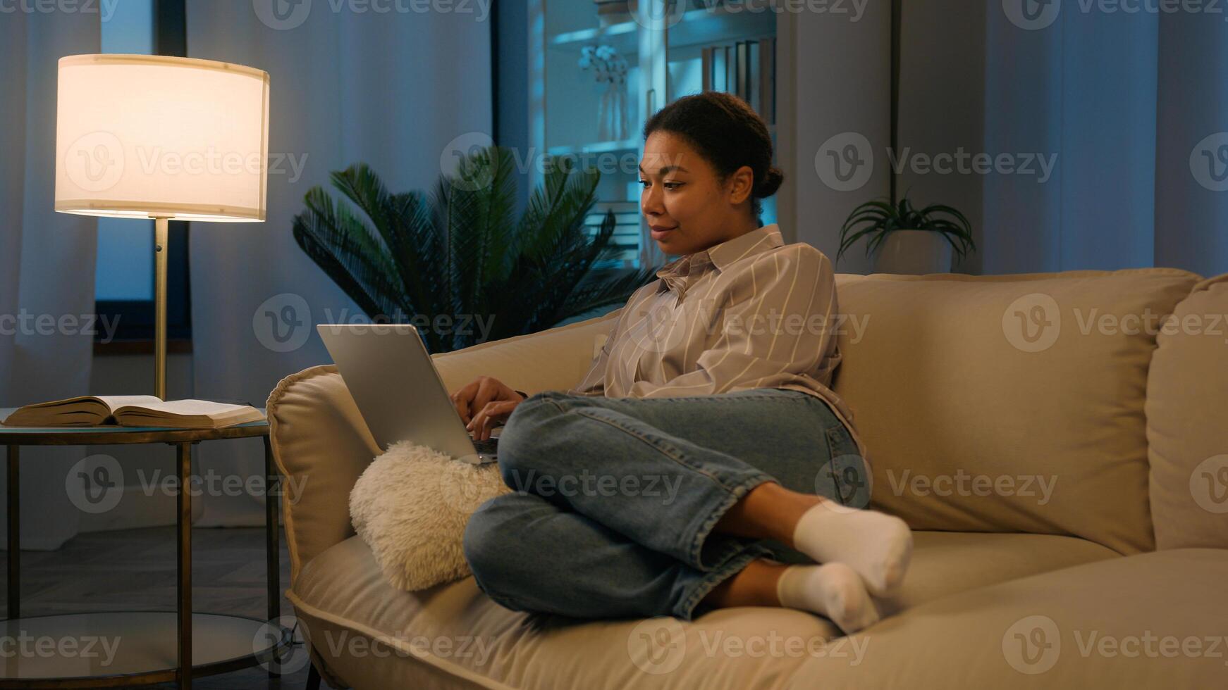 African American woman girl relax on comfortable couch shopping online night time social media addict smiling ethnic female freelancer studying working from home order delivery use laptop application photo
