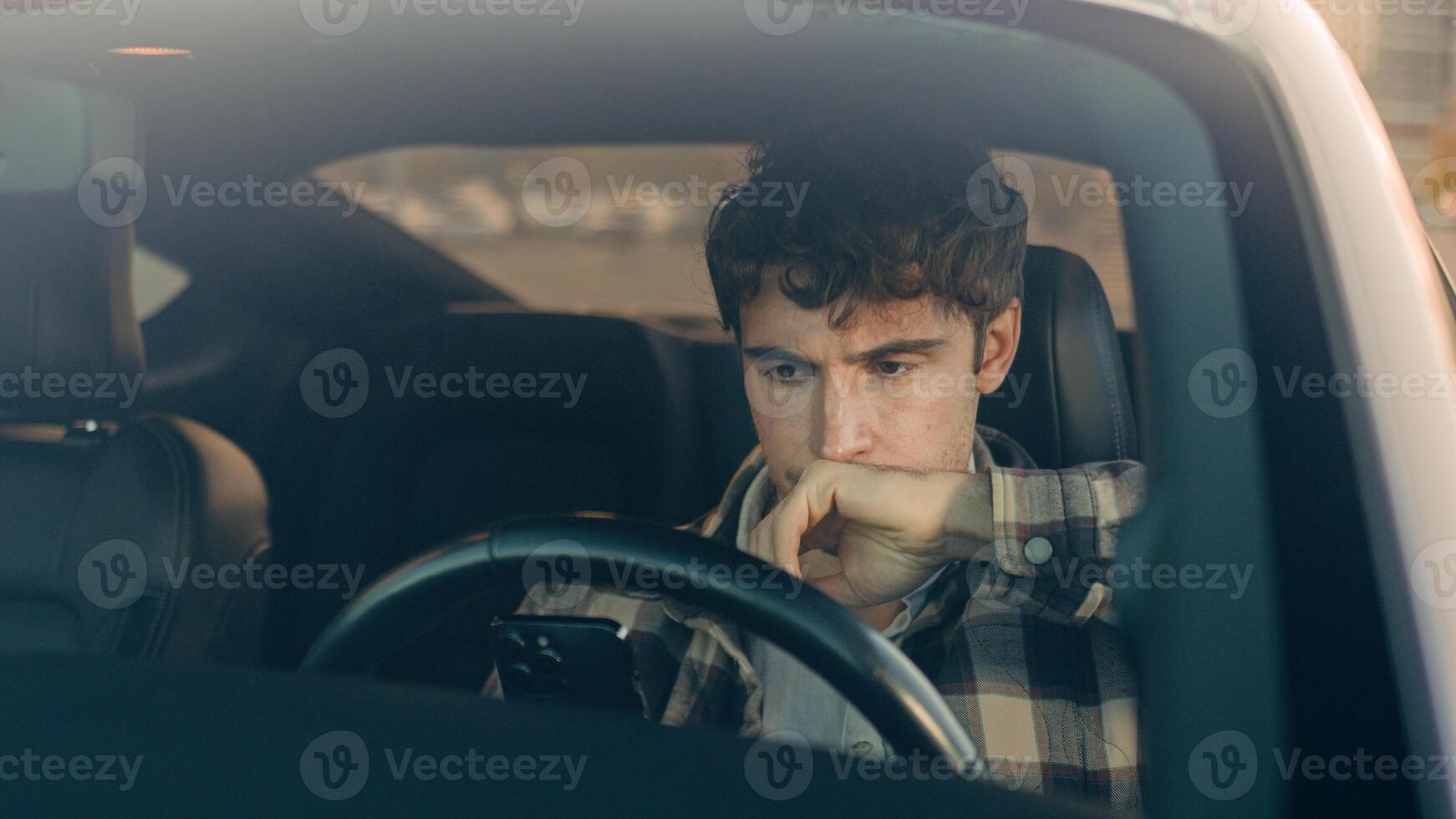 Displeased upset sad Caucasian man guy male driver car owner inside automobile on parking lot using mobile phone problem with smartphone read bad news frustrated anxious millennial driving auto city photo