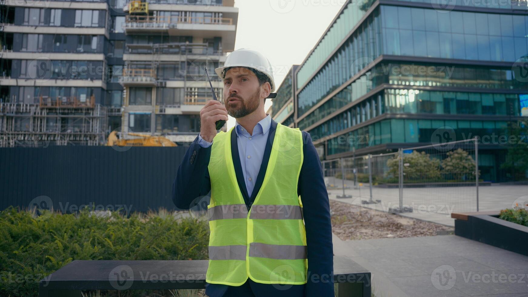 Caucasian builder architect engineer contractor repairman outdoors in city talk with remote radio building urban development industry man worker in helmet hardhat and vest speaking on walkie talkie photo
