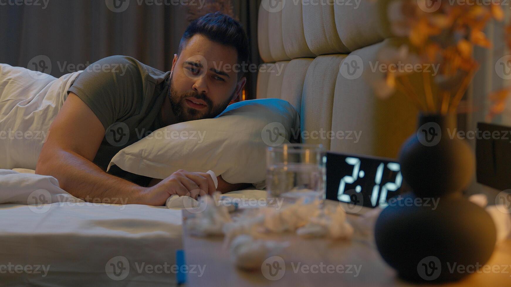 Caucasian man lying on bed suffering sick sneezing insomnia guy male bedroom home unwell blowing allergy illness symptom flu seasonal virus immune unhealthy respiratory infection discomfort exhausted photo