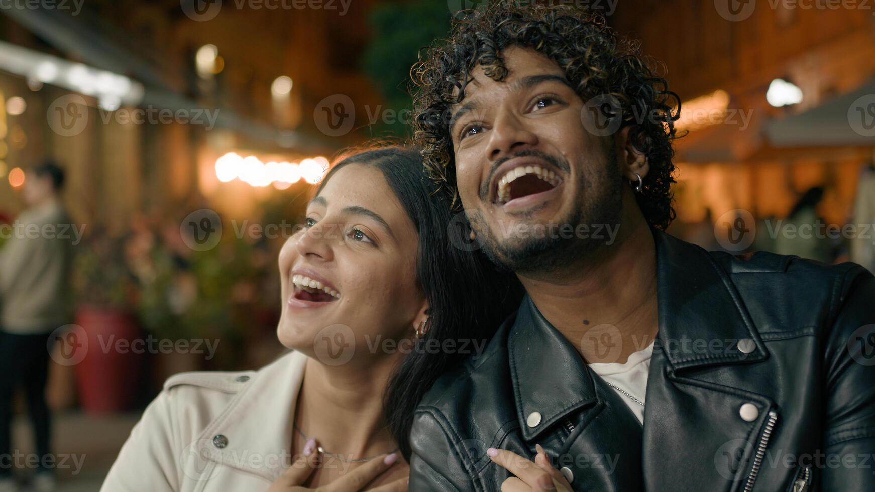 Happy laughing smiling Indian boyfriend man and Arabian girlfriend woman couple travelers tourists in new city contemplate strolling walking cuddling walk at evening night street architecture explore photo