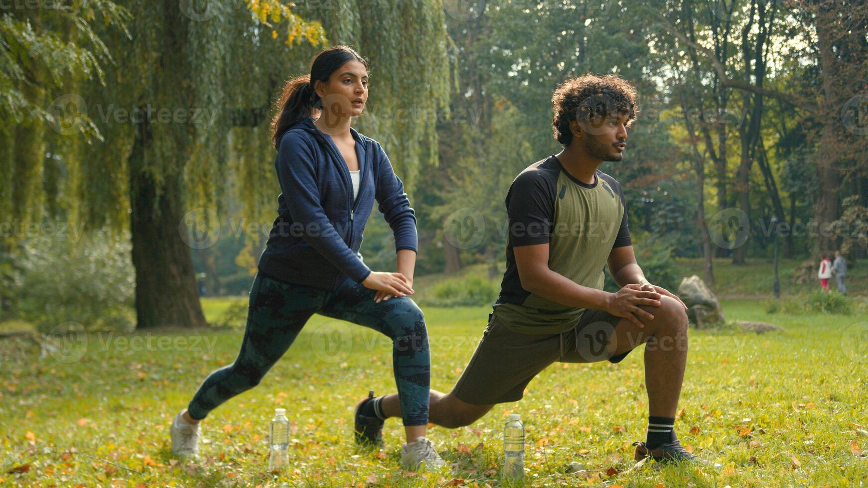 Confident determined Indian couple Arabian man woman girl guy doing lunges squats exercises sport morning workout in park outdoors fit friends people team sports body weight training personal coach photo
