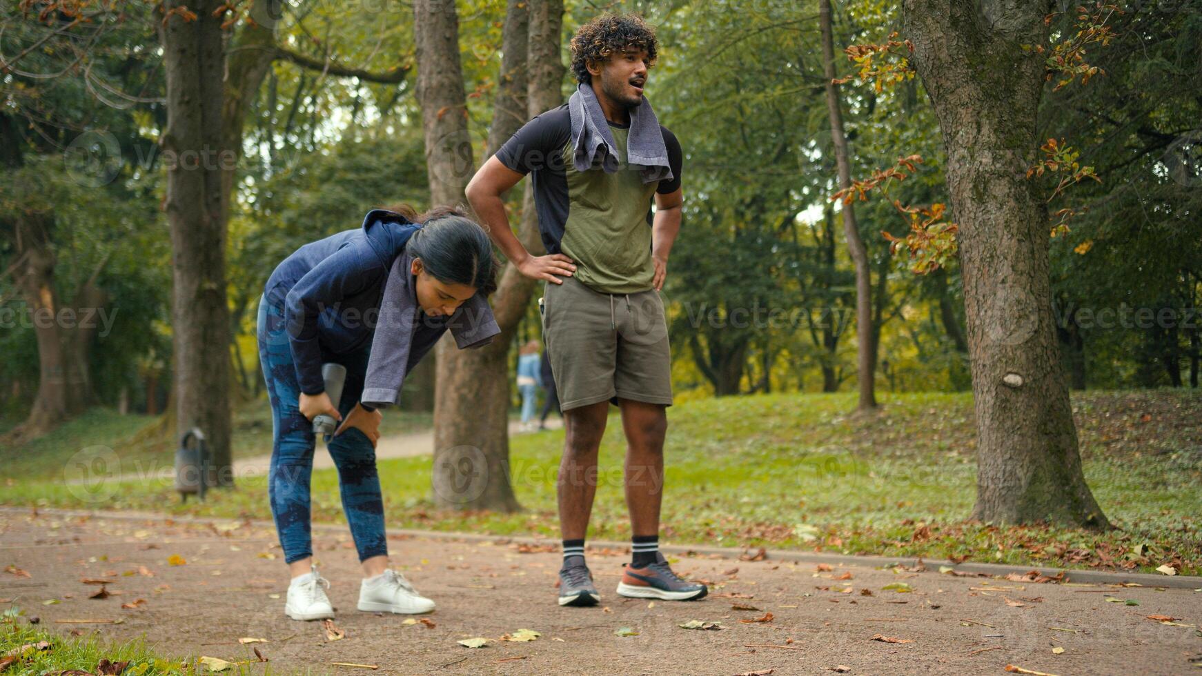 Indian Arabian couple jogging outdoors run together woman man in park stop pause break tired exhausted training activity exercise fitness runners fatigued running workout sport wipe sweat with towel photo