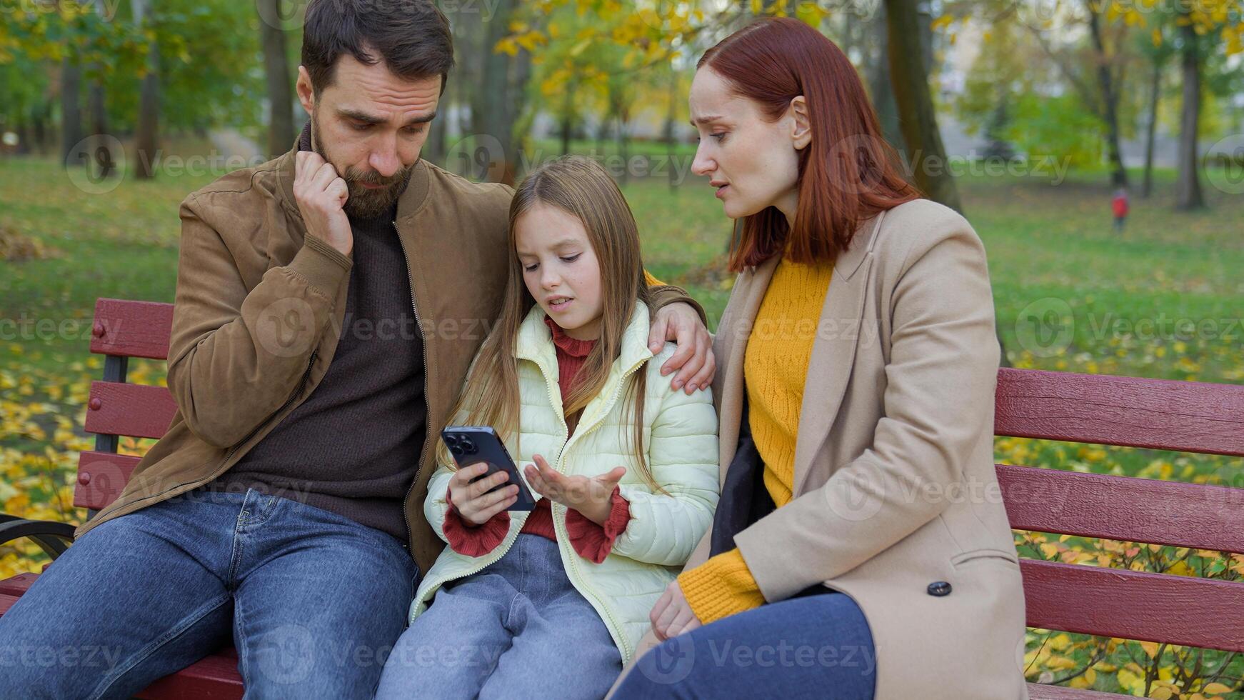 Caucasian family at city bench together outdoors autumn sad upset confused worried with mobile phone bad news smartphone failure little daughter girl child kid with parents mother woman father man photo