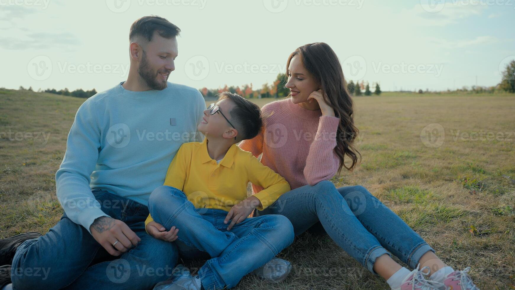 Cute Caucasian happy family portrait joyful man male dad smiling woman female mom little boy child kid son sitting together hug embrace looking camera outside nature field farmland park picnic nature photo