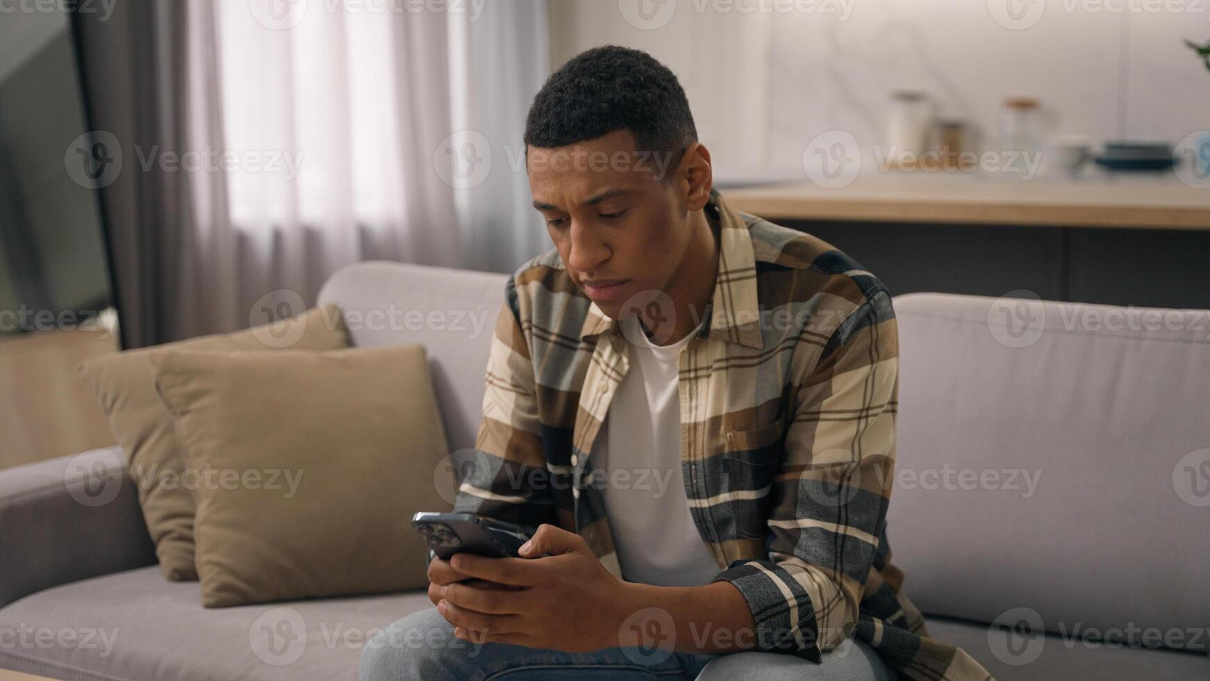 Tired African American man exhausted biracial male worried anxiety ethnic guy stress pensive thinking thoughtful think problem read bad news trouble finish stop browsing mobile phone app at home couch photo