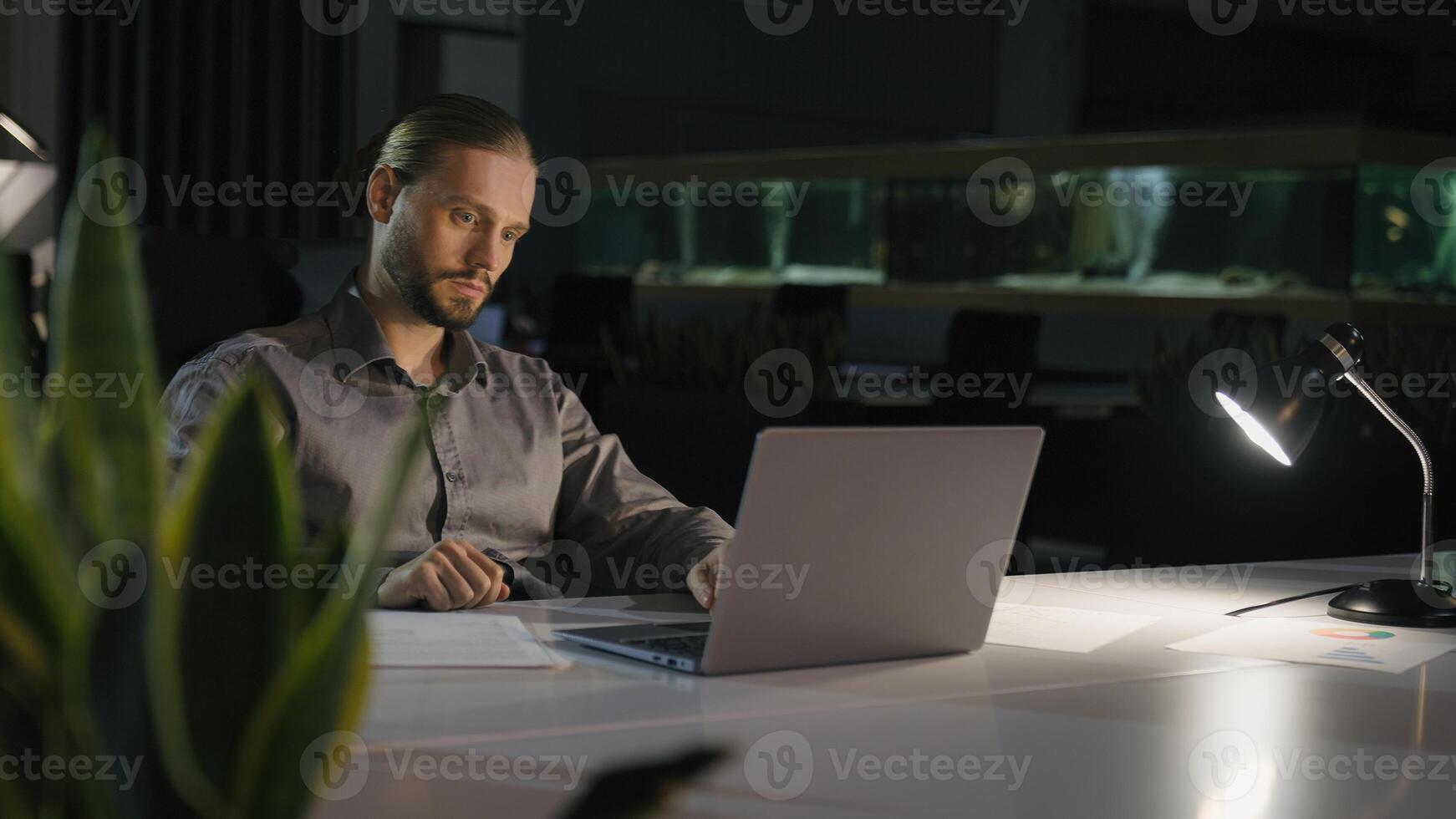 Overtime working businessman manager man at night evening dark office work with laptop serious concentrated business man worker company leader employer with computer job at table workplace late time photo