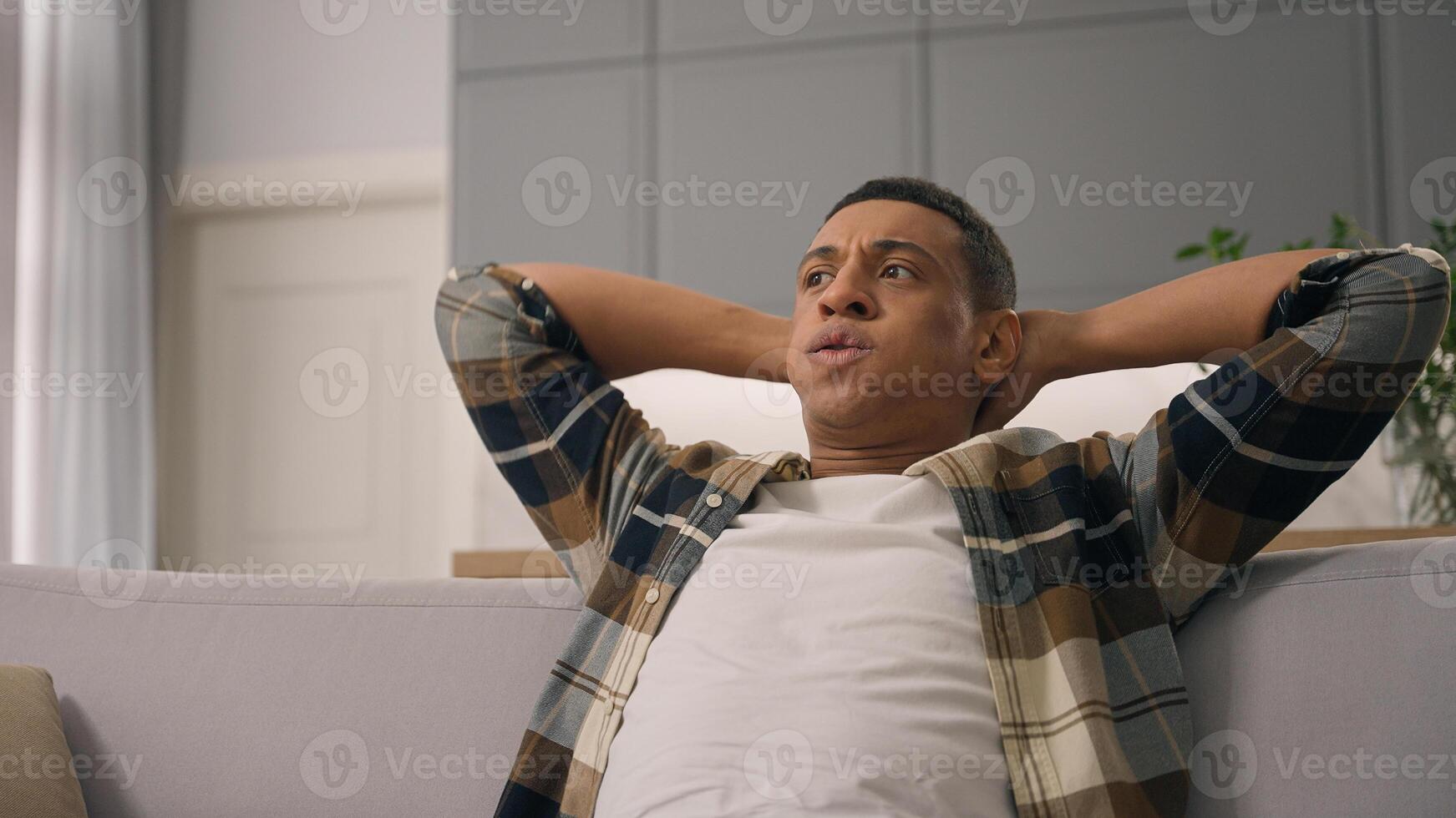 Tired relaxed exhausted African American man ethnic guy male homeowner relaxing on comfortable couch sofa worry anxiety angry fatigue at home apartment own real estate problem stress trouble indoors photo