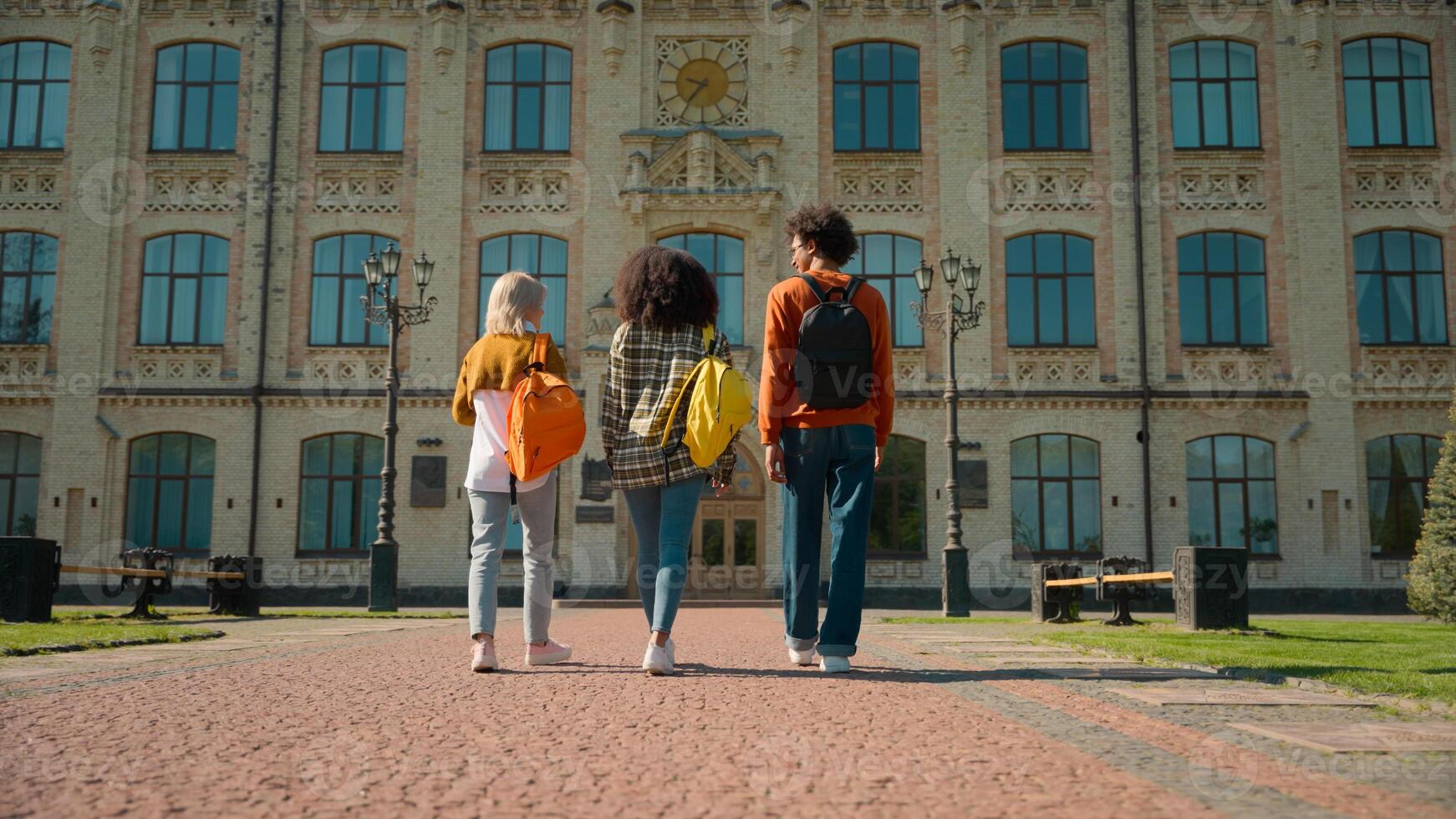 Back view three multiracial people outside go to class lesson studying together students diversity friends man guy male Caucasian African females women girls walking outdoor school university college photo
