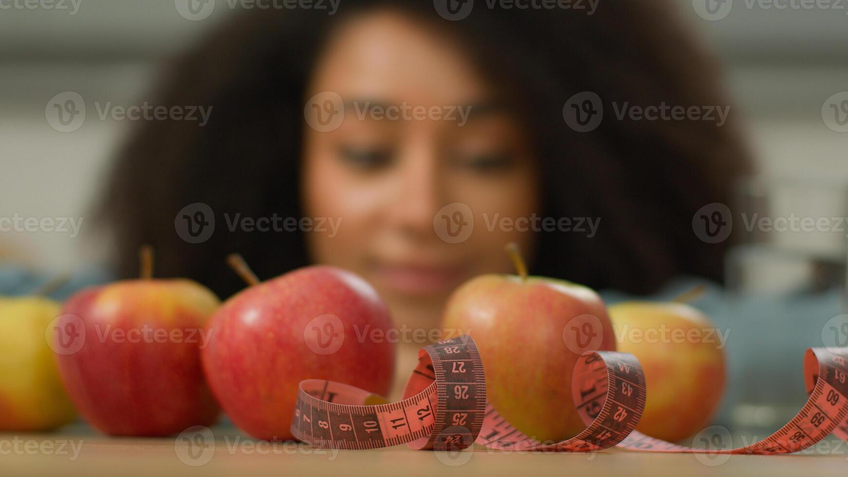 Happy health smiling African American woman ethnic girl female at home kitchen looking enjoying fruits apples glass of water measuring tape at table weight control diet healthy nutrition dieting slim photo