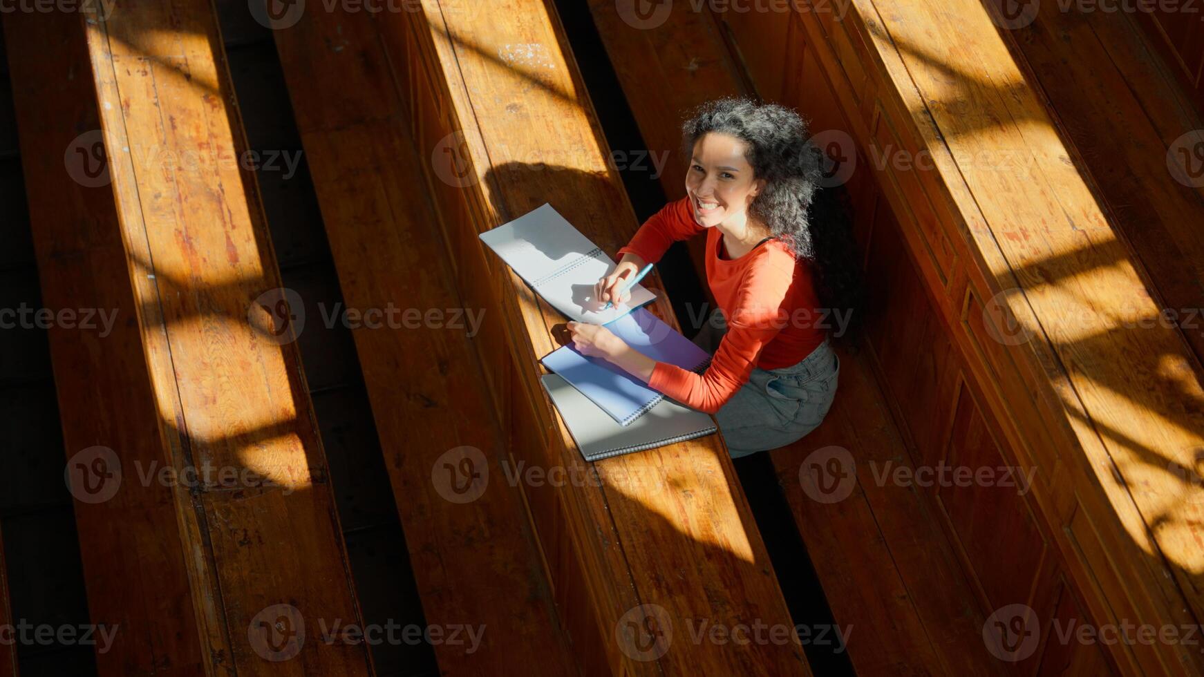 Top view from above woman girl student female study at table writing studying learning write learn course copybook in empty sunny shadows class college university auditorium looking at camera smiling photo