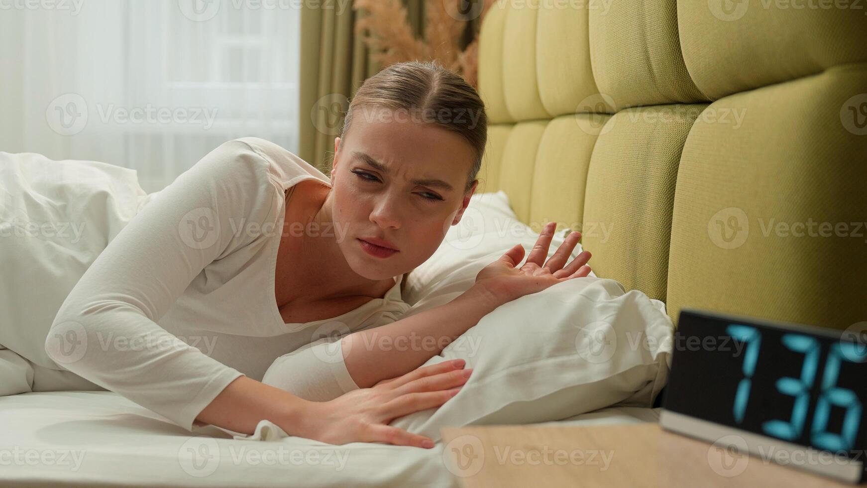 Tired sleepy fatigued girl wake up in early morning bed home bedroom stressed dissatisfied upset lazy time go work insomnia health problem sleep disorder woman female lady loud ringing of alarm clock photo