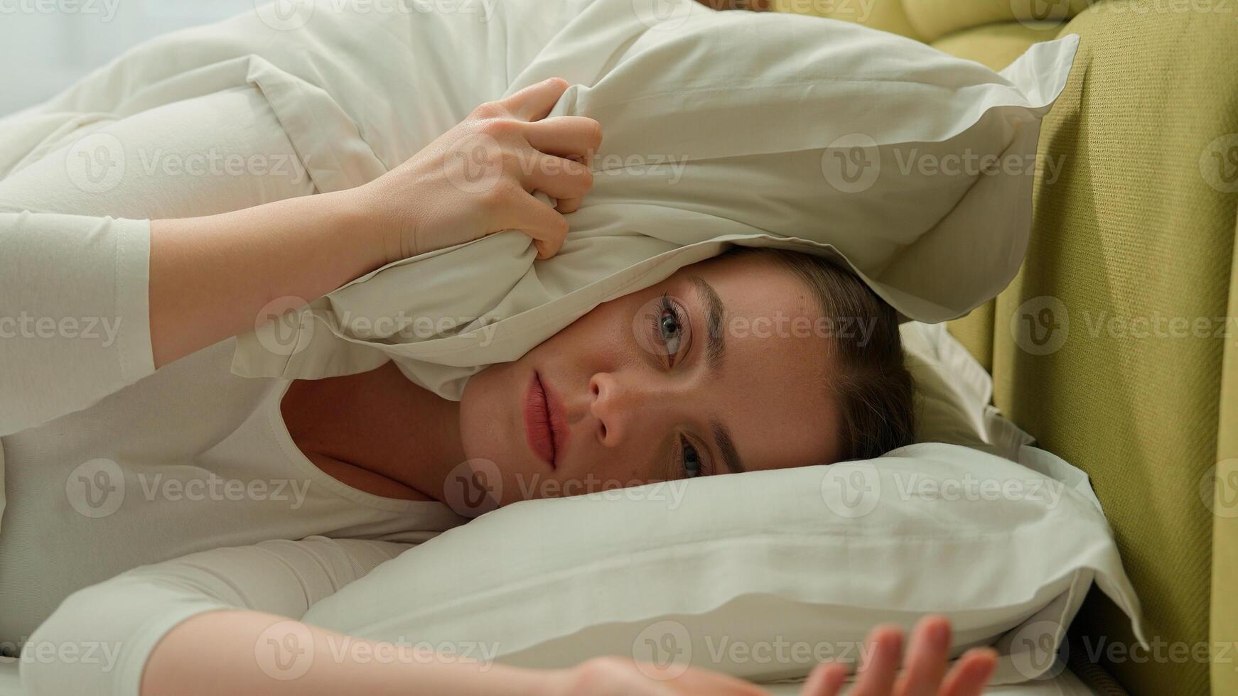 Tired sleepy girl wake up in early morning bed home stressed insomnia health problem sleep disorder woman female lady loud ringing of alarm clock check time cover head with pillow noisy neighbors photo