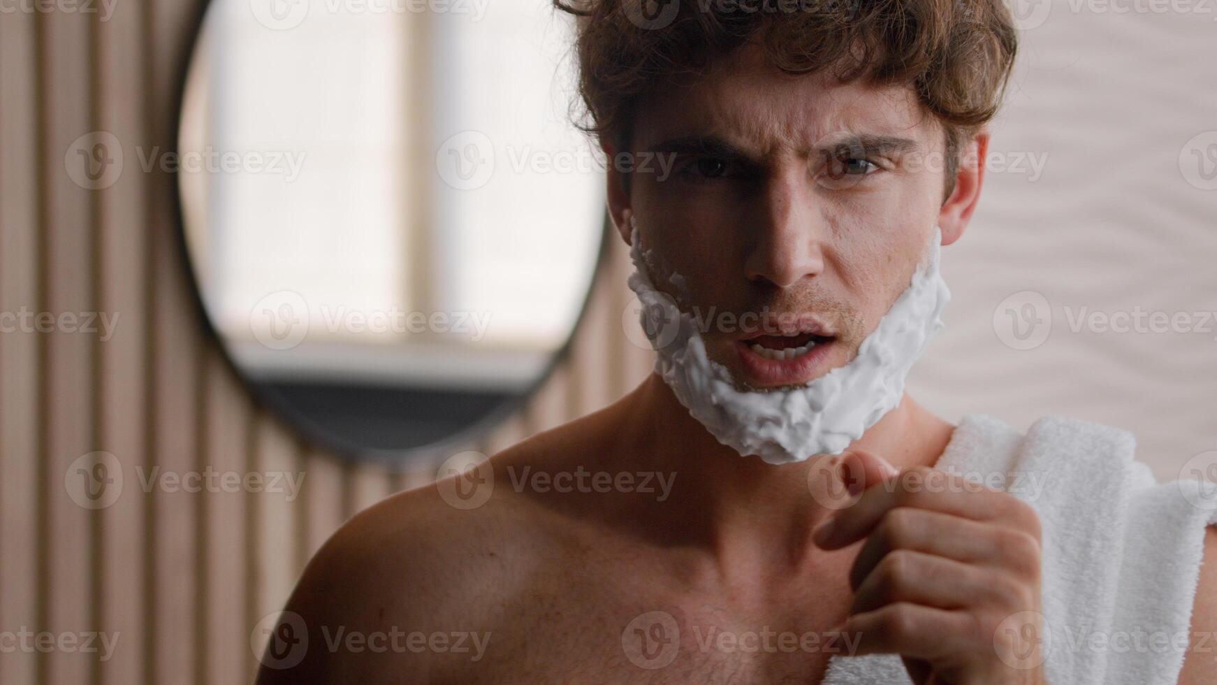 Funny happy Caucasian millennial silly man singing in shaving razor blow dancing active fooling with foam on beard foamy bearded with shave gel sing song dance having fun listening music in bathroom photo