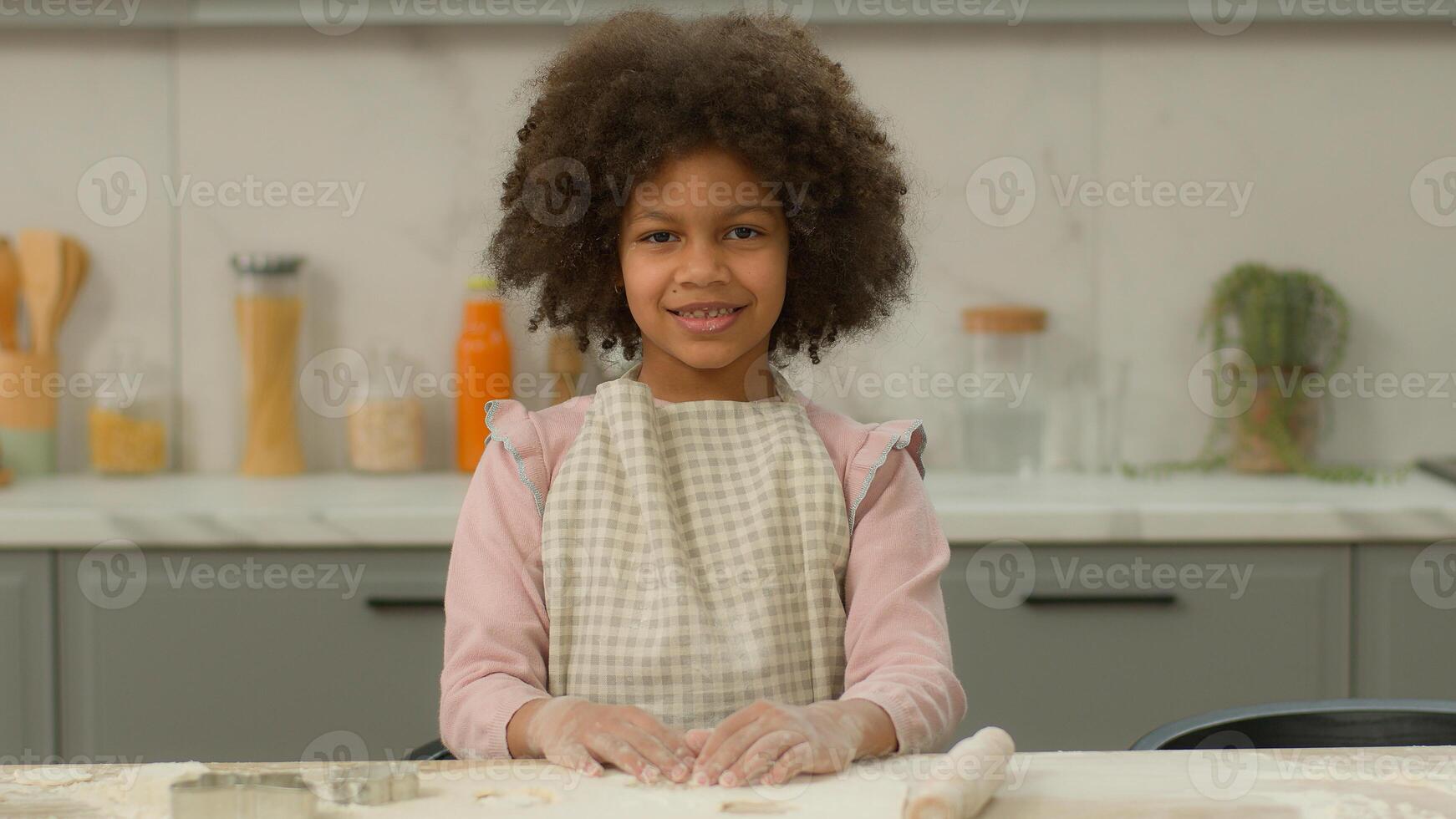 Portrait happy smiling little African American girl in apron alone smile positive child kid ethnic daughter posing near table cook baking cooking in kitchen home flour dough recipe looking at camera photo