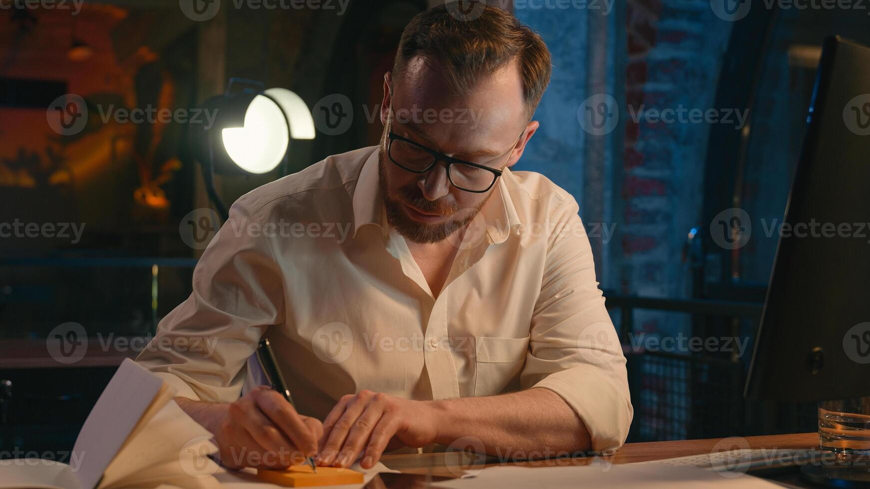 Caucasian man business guy businessman male in dark night evening office work with computer pc online paperwork writing notes on sticky paper note hide on monitor screen reminder internet task working photo