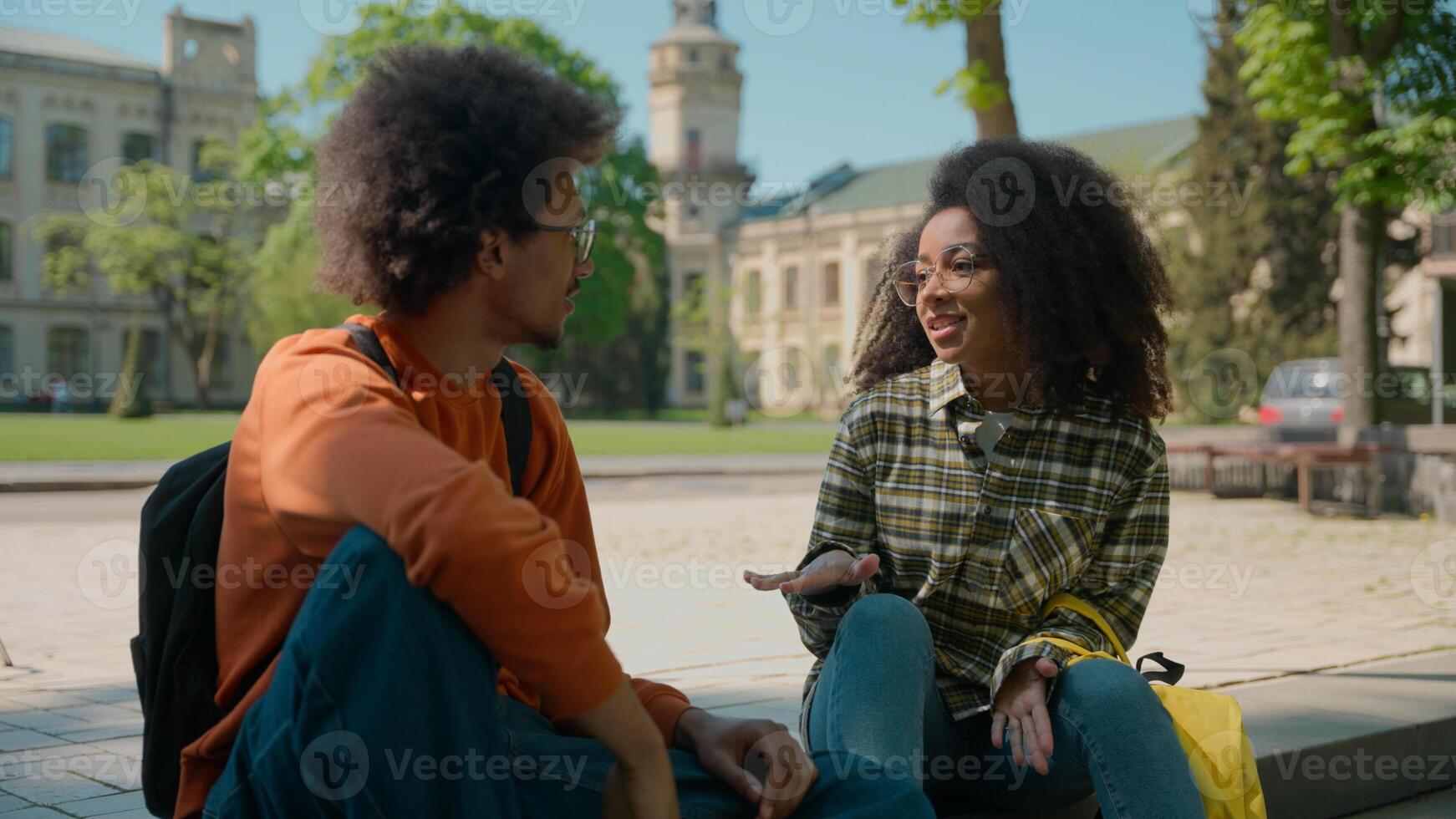 African American ethnic couple students people pupils classmates woman girl lady female man male guy sit outdoors in city talking friendly communicate conversation talk university college high school photo