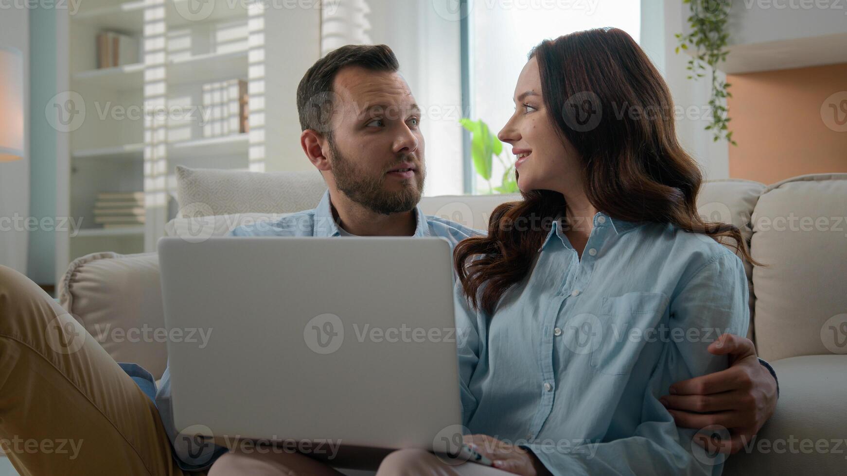 Happy young couple using laptop for ecommerce doing online shopping with shop app together at home Caucasian man and woman looking at computer buying searching in internet booking trip tickets choose photo