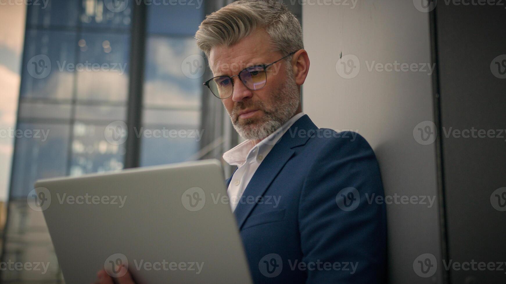 Mature concentrated senior middle-aged employer entrepreneur busy businessman trader old retired business man put on glasses working looking at laptop computer analyzing data online trading in city photo