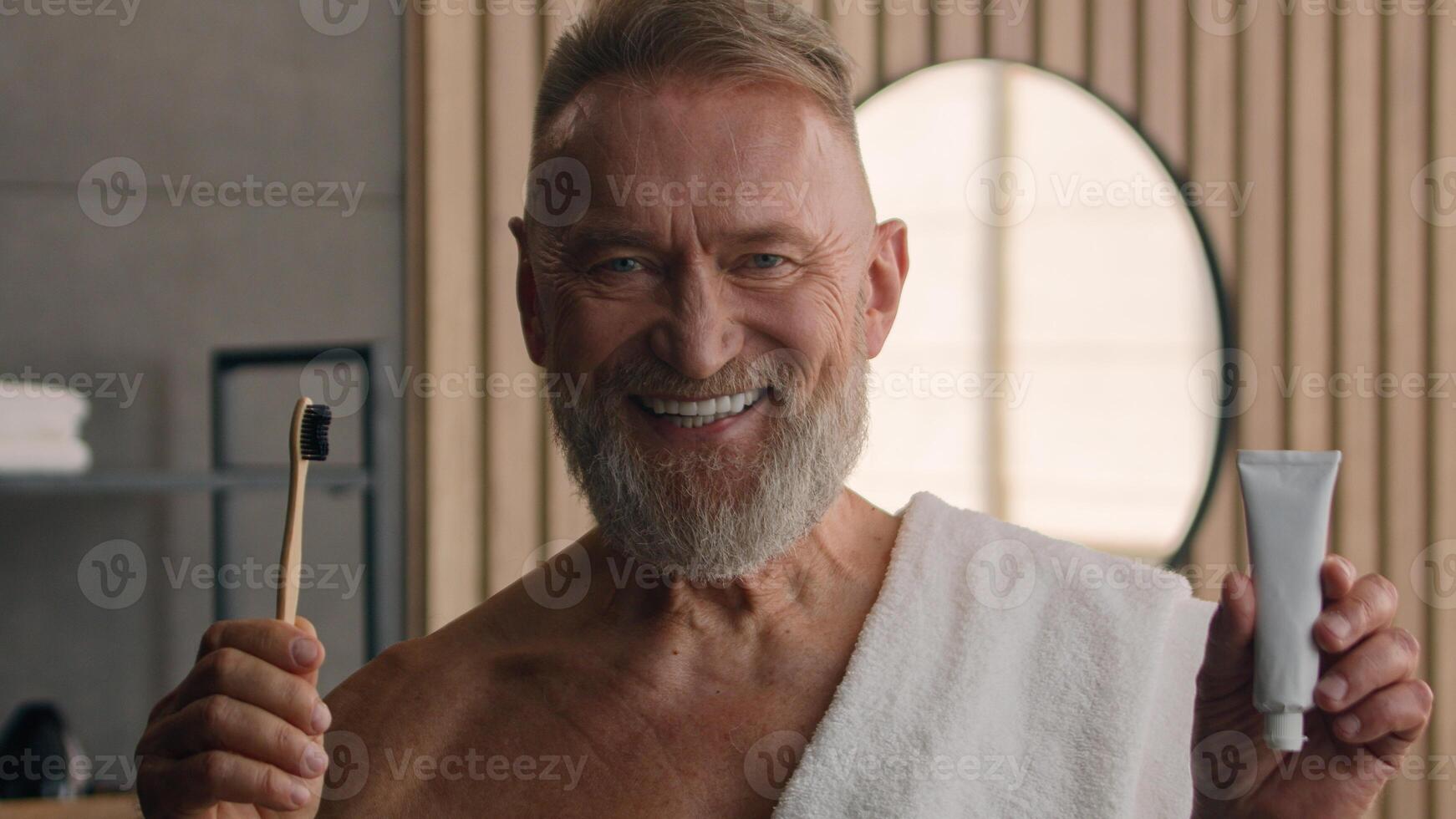 Portrait close up indoors smiling old man bearded grandpa healthy toothy smile looking at camera happy senior male retired mature pensioner in bathroom holding teeth brush and toothpaste dental care photo