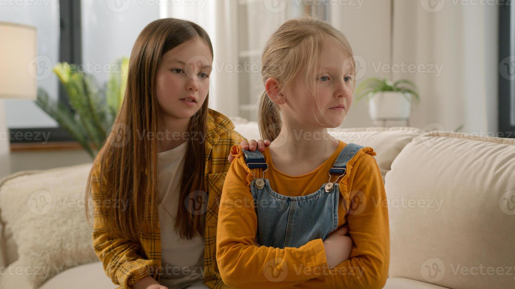 Upset angry little Caucasian children girls sisters kids friends quarrel daughters apology ask for forgiveness feeling guilty touch calming down offended ignore family argument problems at home couch photo