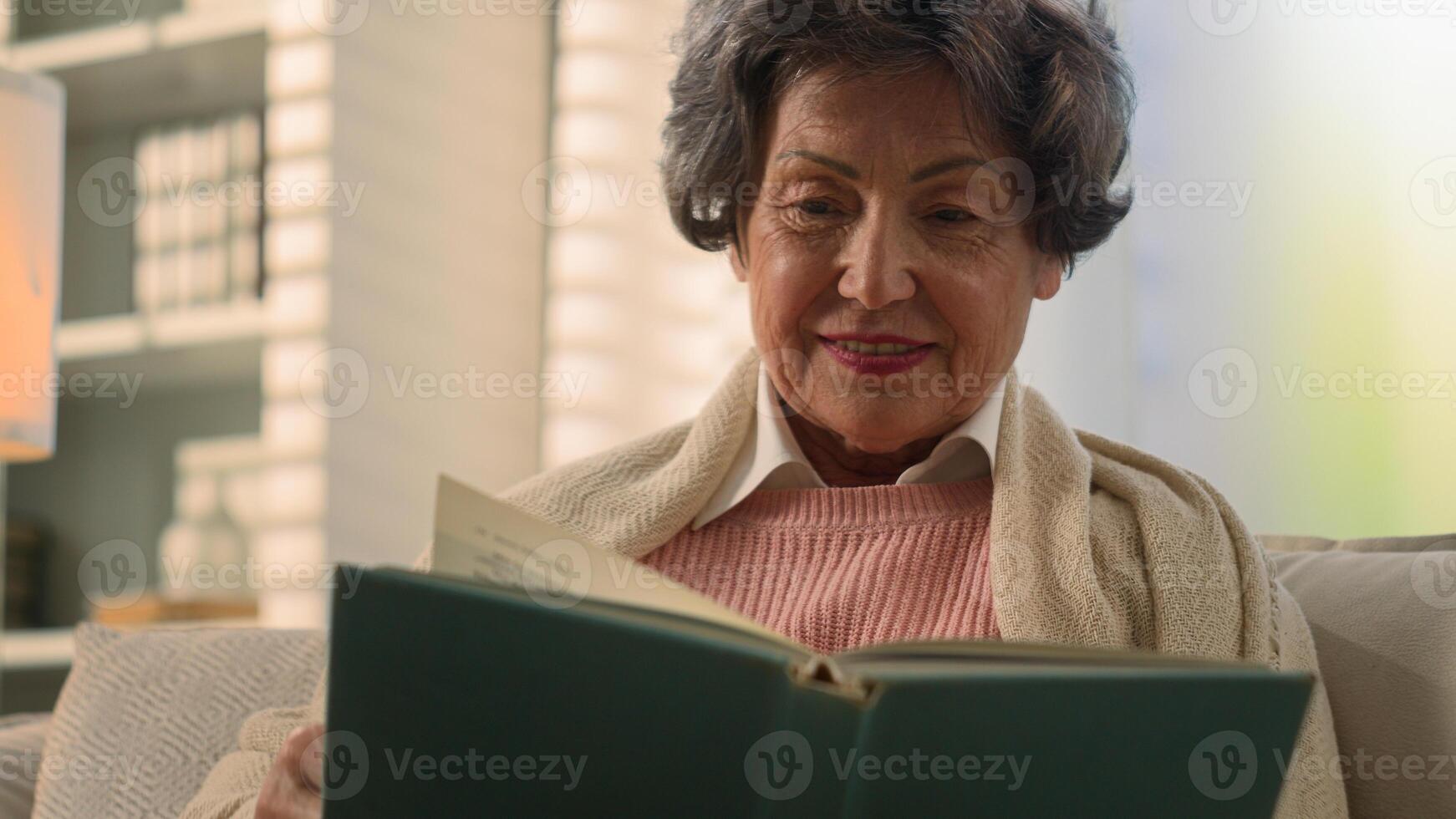 Happy inspired Caucasian old woman reading book smiling nostalgic senior mature lady elderly female retired pensioner grandmother read at home couch watching photos in album memory remember nostalgia