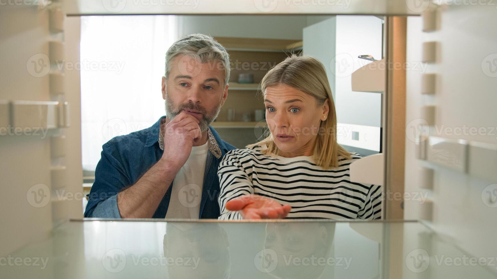 Point of view POV from inside refrigerator Caucasian adult family mature couple middle-aged man woman open empty fridge have nothing to eat sad upset with poor poverty unemployment starvation hunger photo