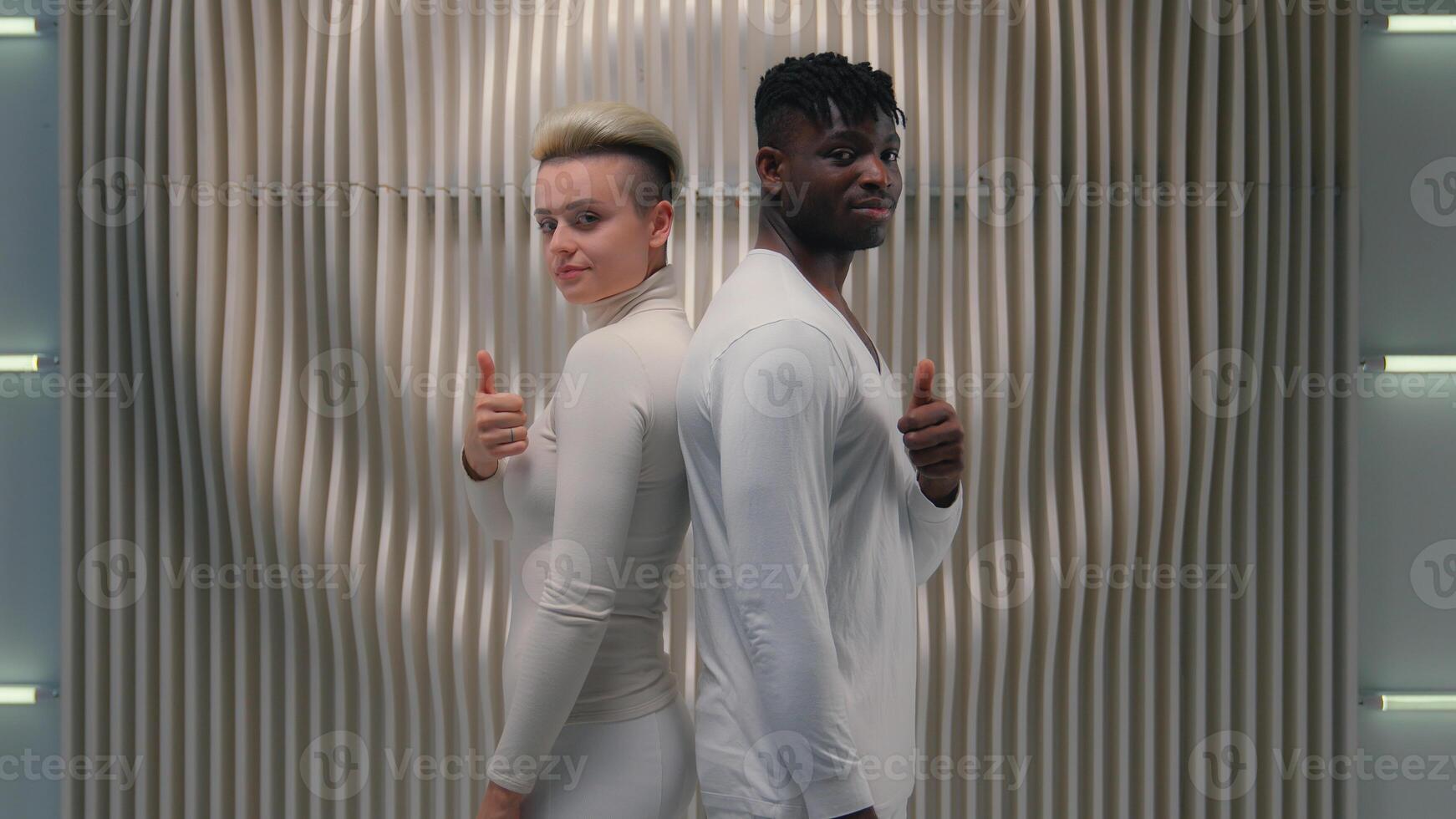 Two multiracial people metaverse cyber gamers futuristic Caucasian girl female woman posing together African American male guy man showing thumb up recommend looking camera cyberspace futuristic game photo