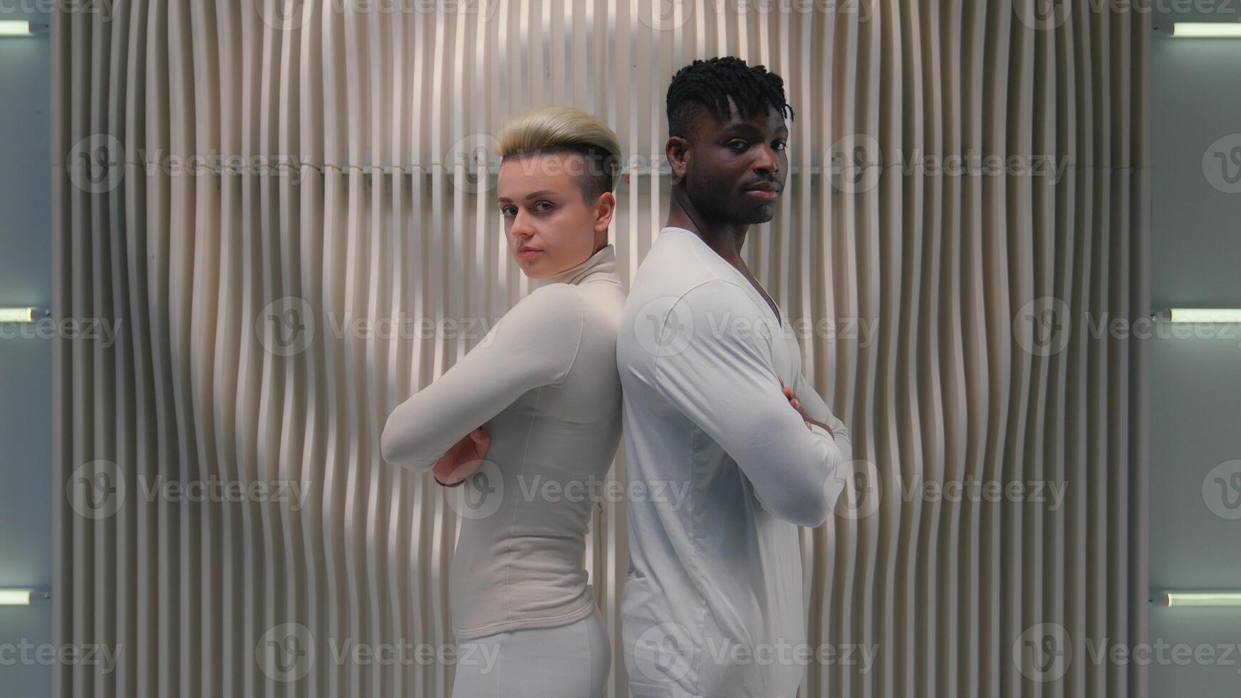 Two multiracial people metaverse cyber gamers Caucasian girl female lady woman posing together with African American male guy man crossed hands standing looking at camera cyberspace futuristic game photo