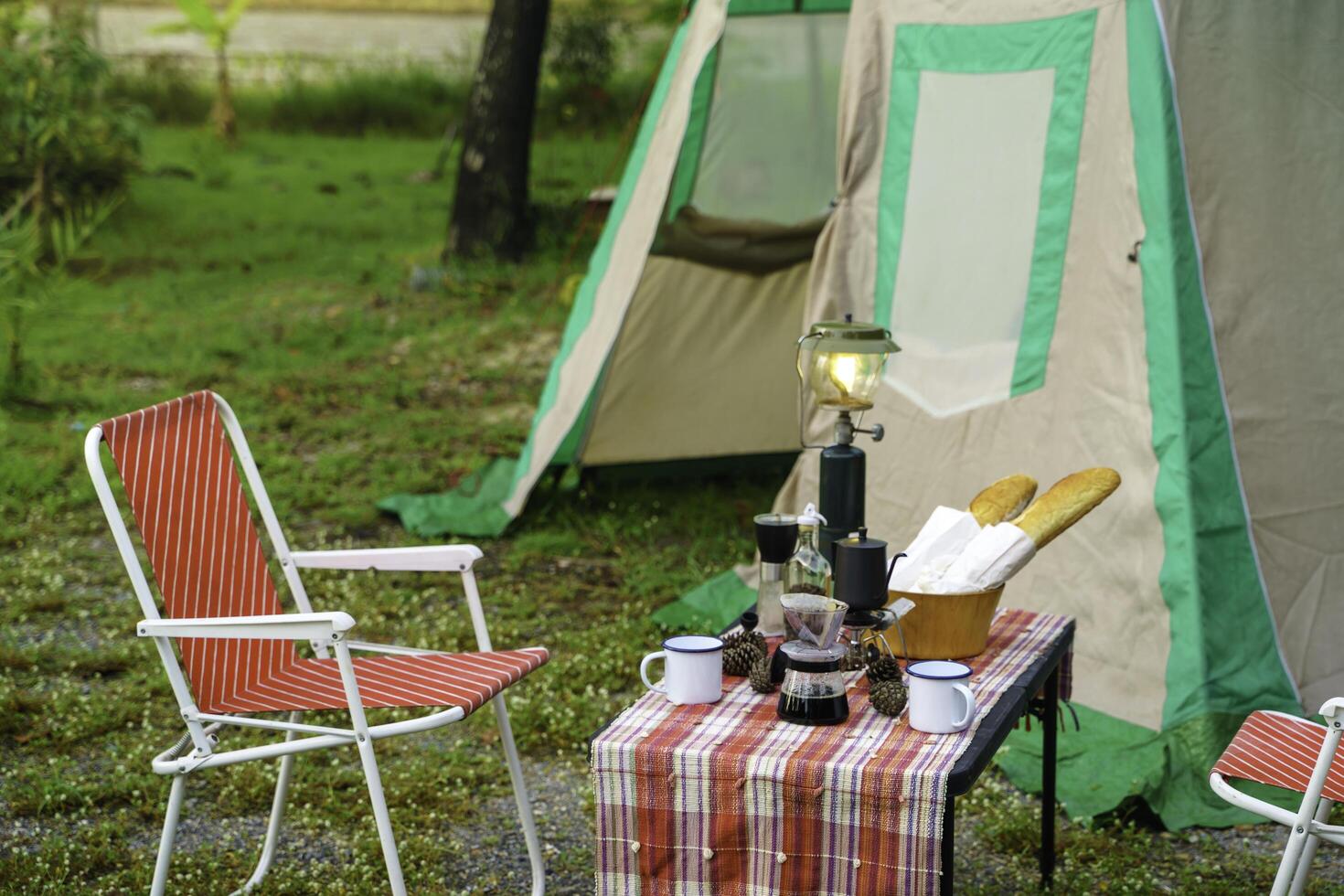 selective focus of Vintage drip coffee set and baguette on a table in front of a camping tent in the forest in the morning, soft focus. photo