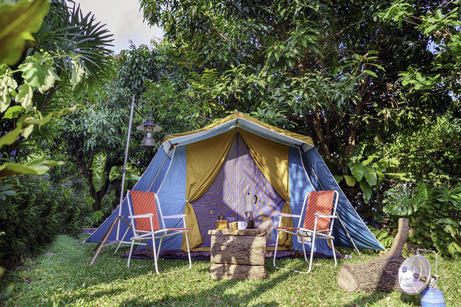 Camping tents at night, vintage cabin tents, antique oil lamps, retro chairs, and a group of camping tents with outdoor coffee-making facilities on wooden tables in a forest camping area in the forest photo