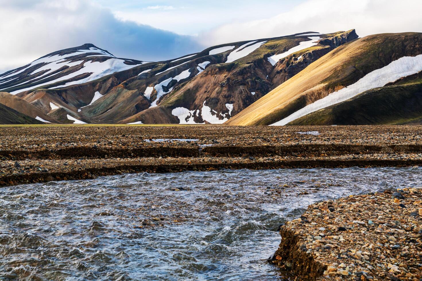 Stream flowing in front of snow covered mountain. photo