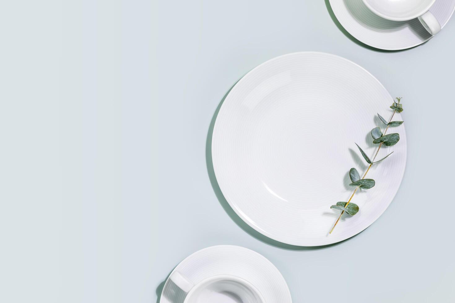 Empty dishes and cups with eucalyptus twig on blue background with copy space photo