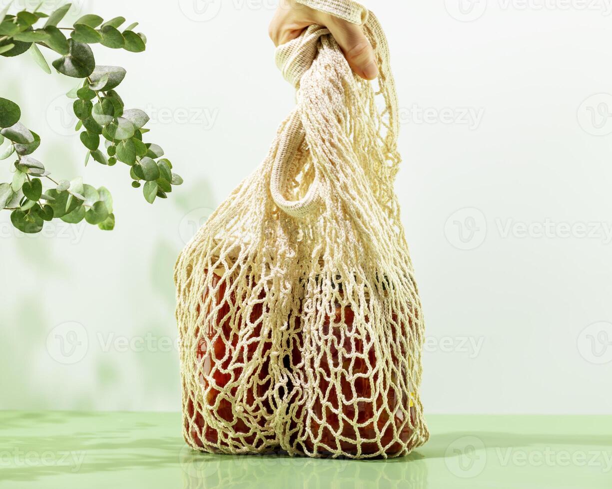 Hand is holding mesh shopping bag with glass bottles with fermented vegetables photo