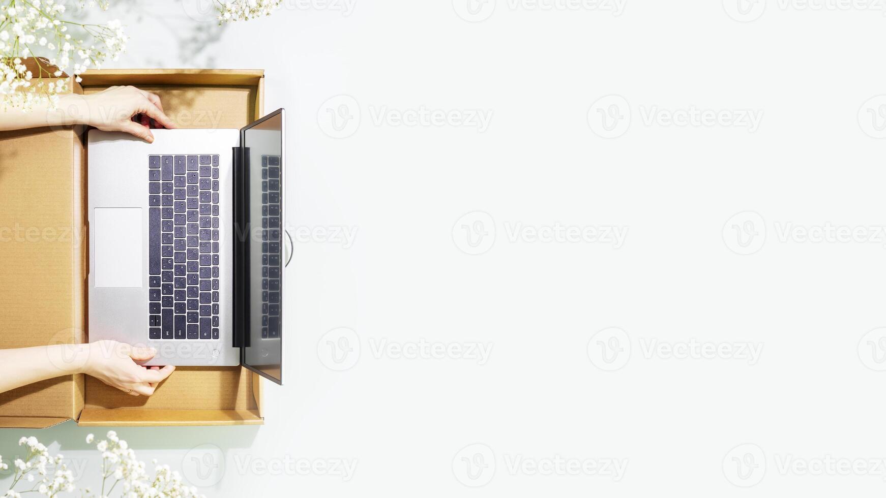 Womans hands holding laptop in cardboard box on blue background with copy space photo