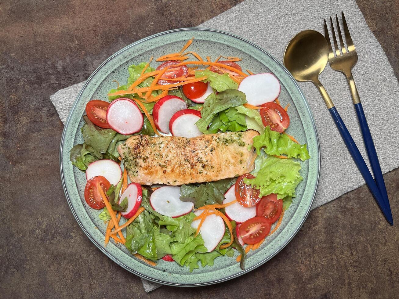 A perfectly cooked salmon fillet with a herb crust, served on a bed of fresh greens with cherry tomatoes and radishes with golden spoon on rustic table photo