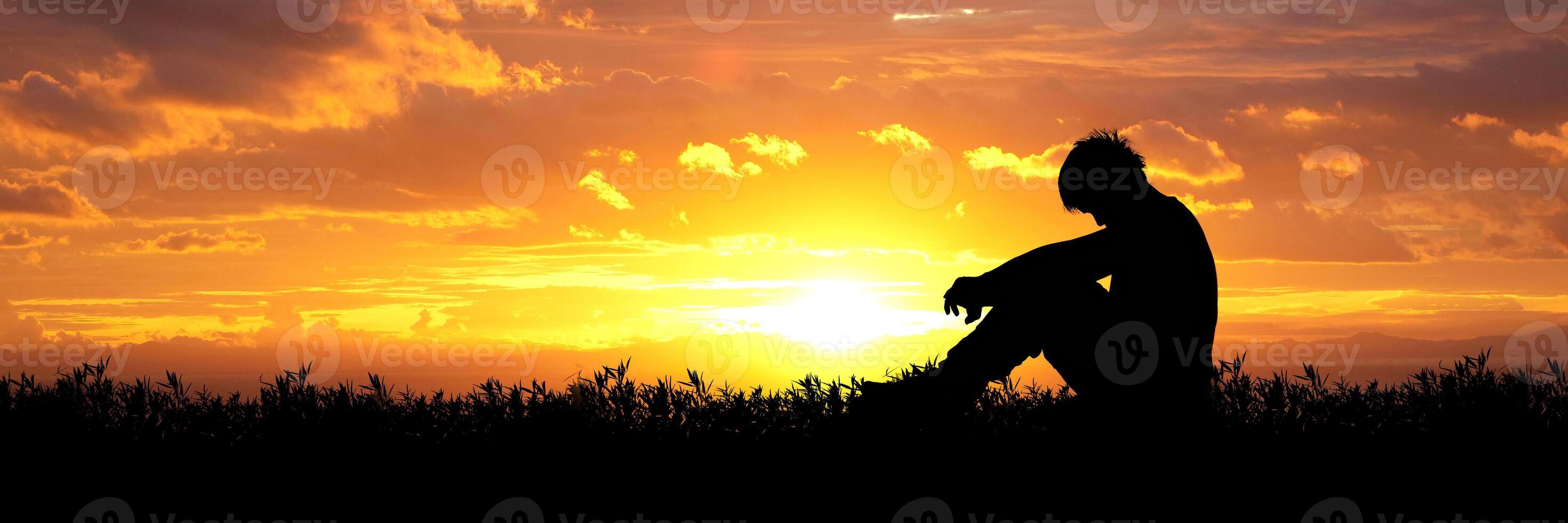 Silhouette of a Person Sitting in a Field at Sunset with Vibrant Orange and Yellow Sky photo