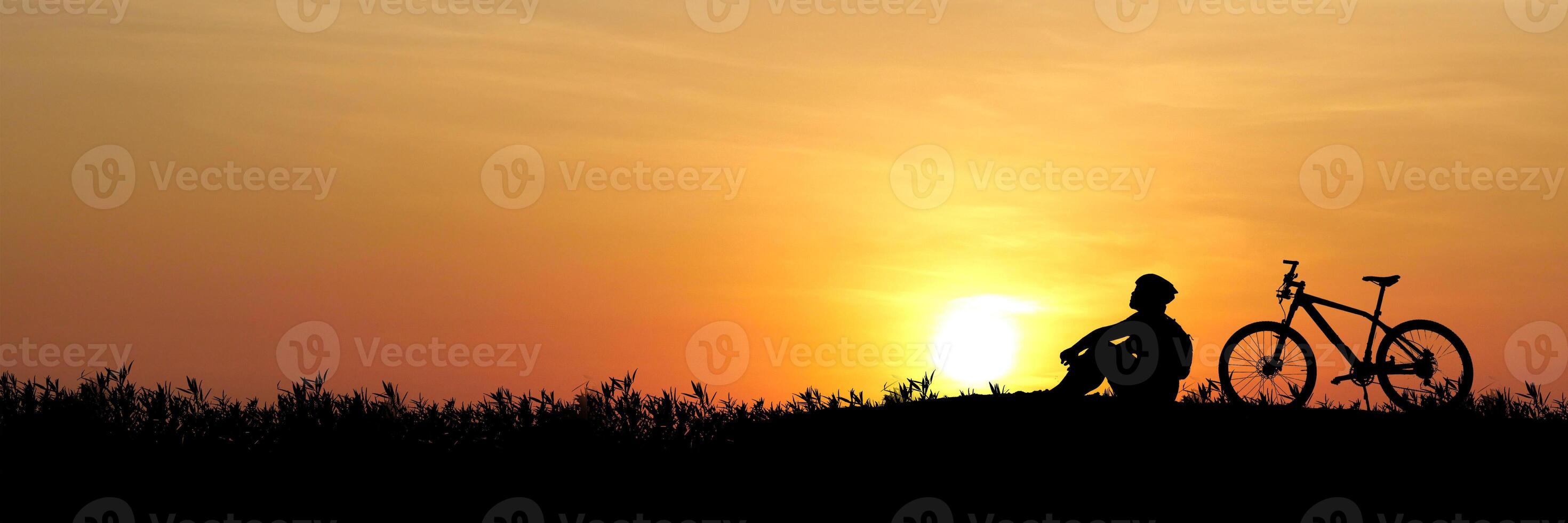 Silhouette of a Person Sitting Next to a Bicycle at Sunset in a Tranquil Outdoor Setting photo