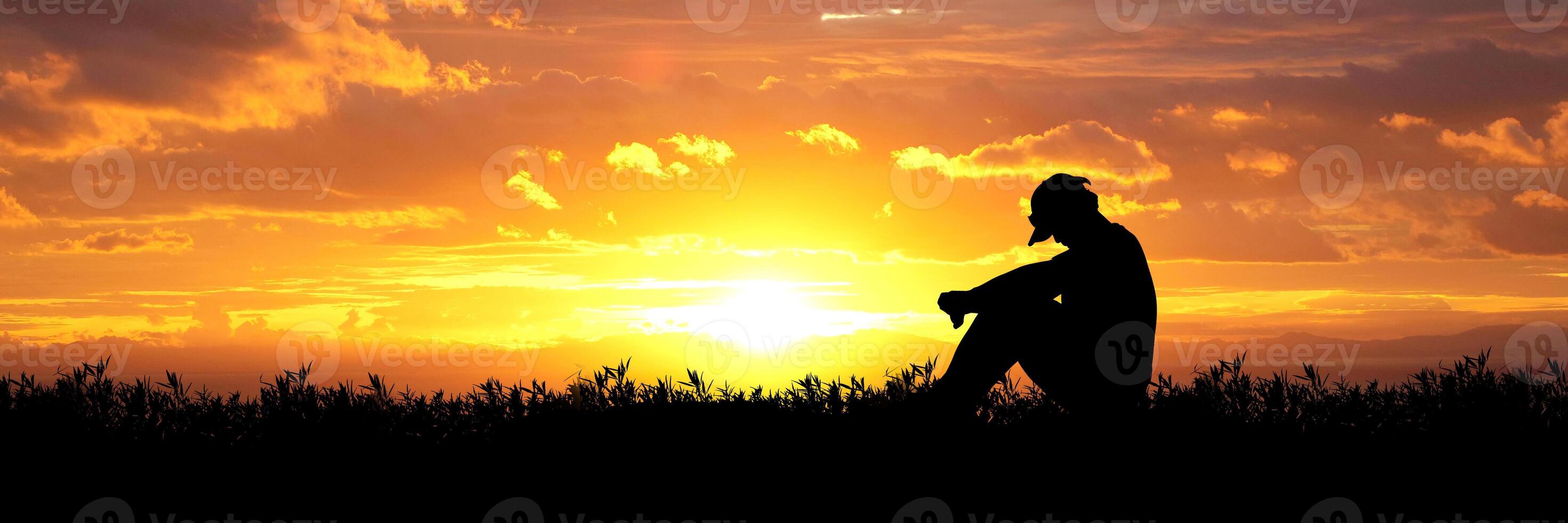Silhouette of a Person Sitting in Nature During a Vibrant Sunset with Golden Sky and Clouds photo